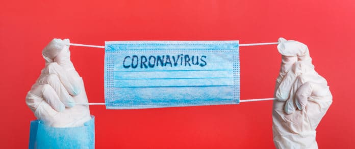 mani con guanti che tengono una mascherina chirurgica con la scritta coronavirus